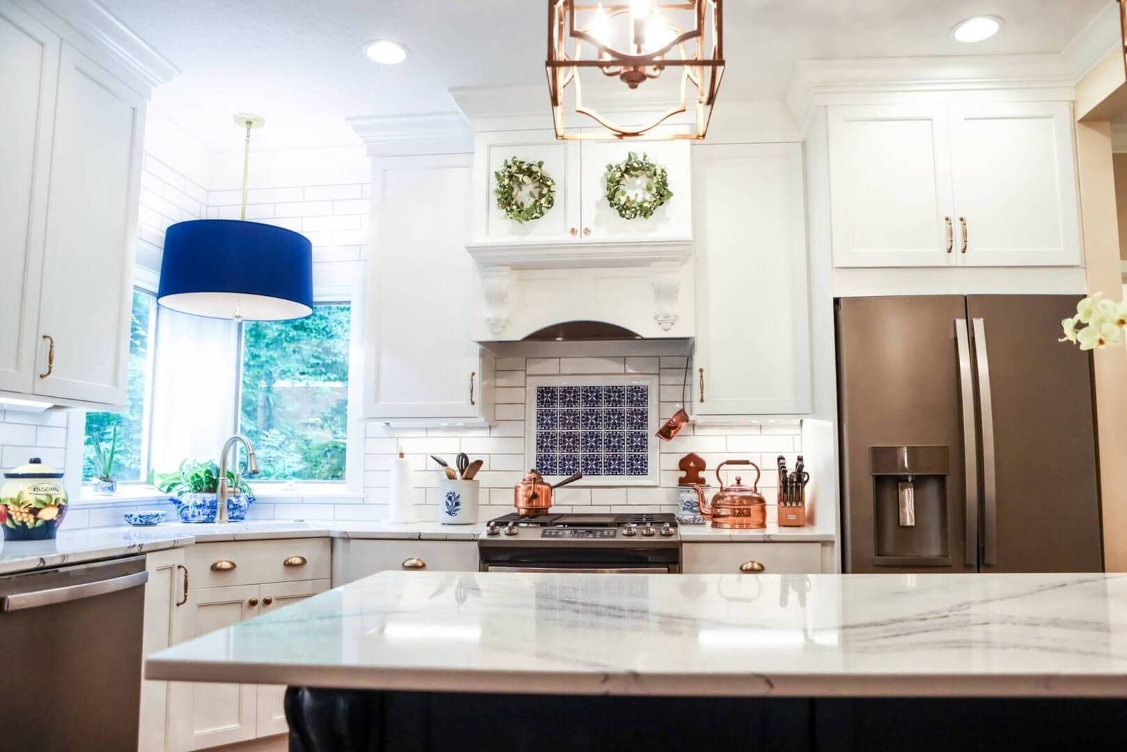wide shot of finished rennovated kitchen with white cabinets, marble countertops and blue/white china