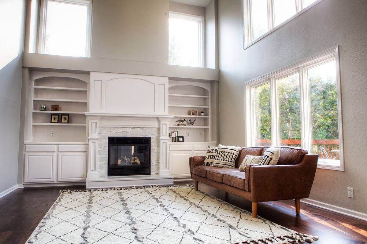 Living room with high ceilings and several windows. Decorated with a leather sofa and area rug. Has a fireplace with built-ins on both sides